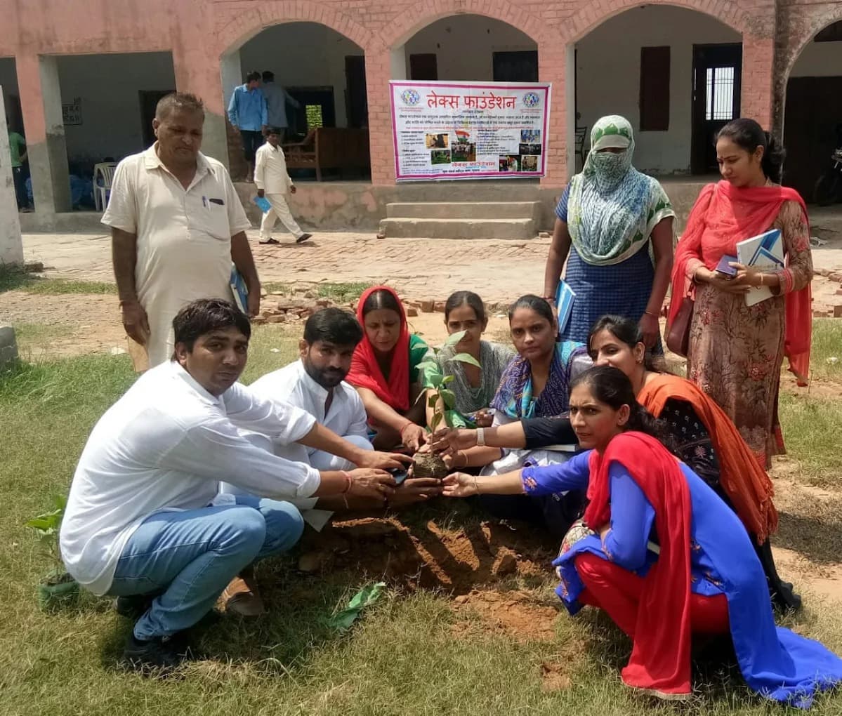 Volunteers and community members planting a sapling together outdoors.
